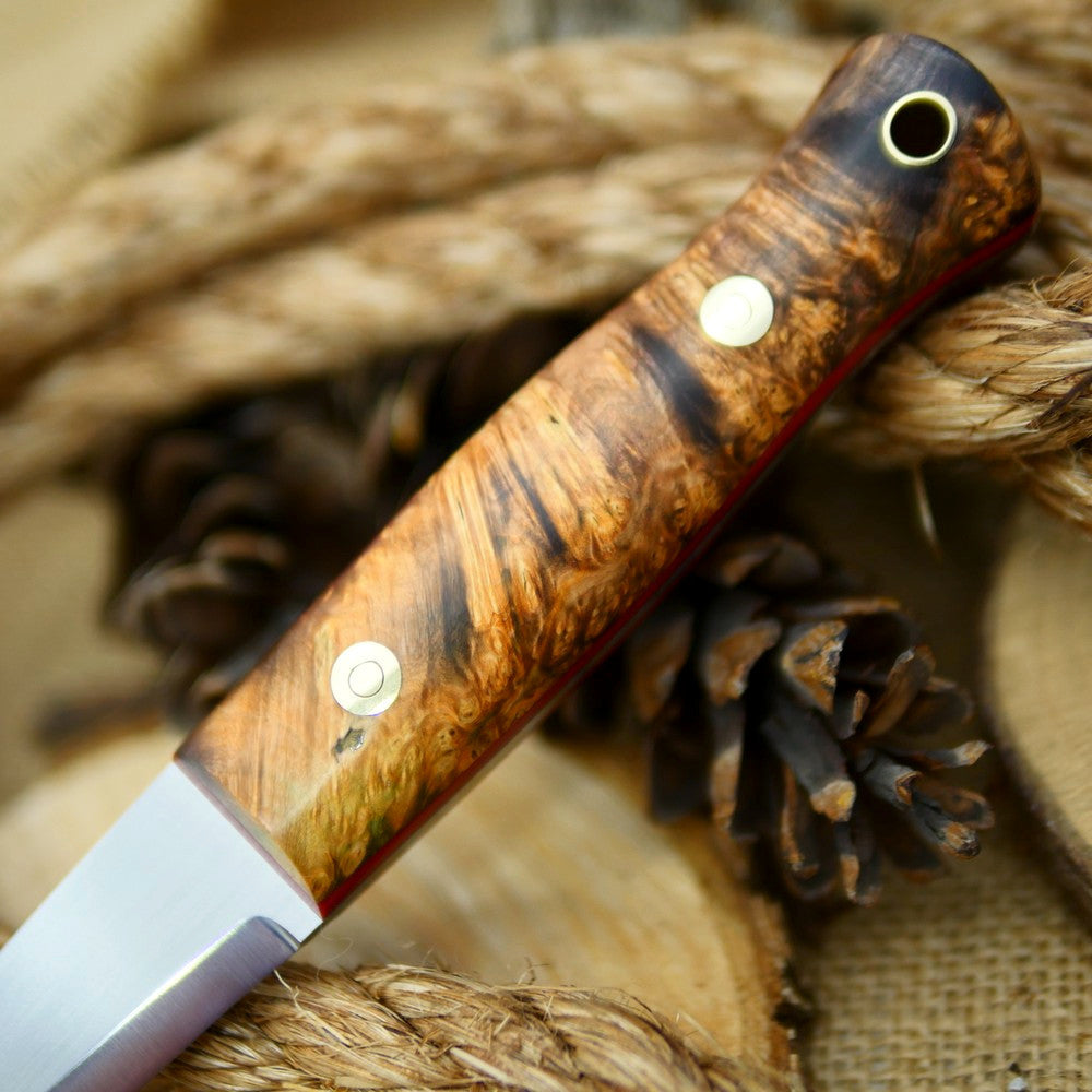 An Adventure Sworn Woodcrafter Bushcraft Knife with dyed box elder handle scales and 1/8 thick red liners