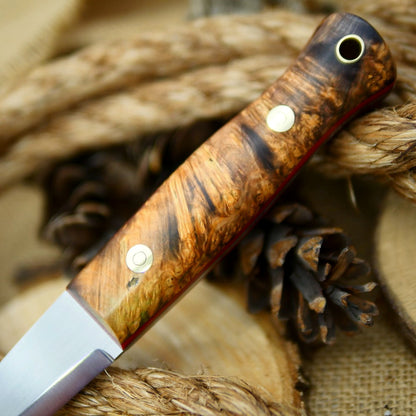 An Adventure Sworn Woodcrafter Bushcraft Knife with dyed box elder handle scales and 1/8 thick red liners