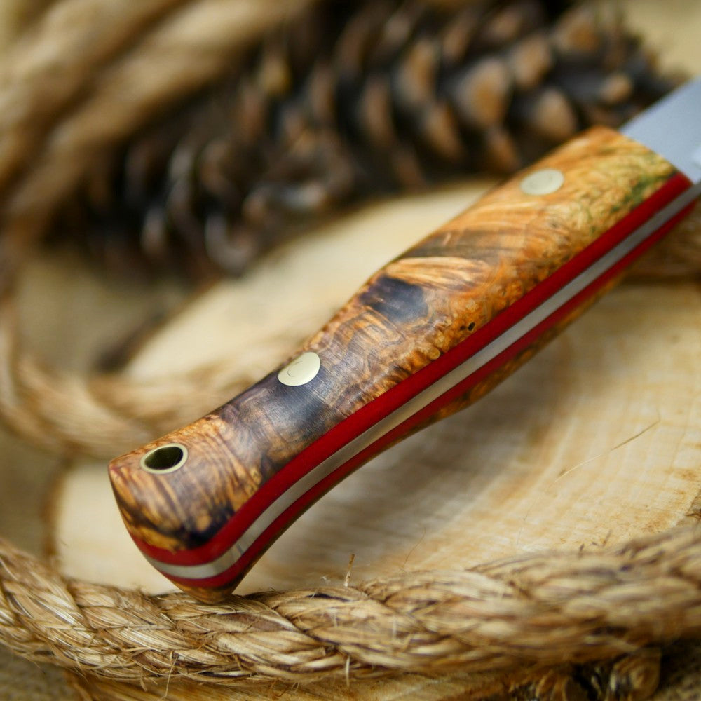 An Adventure Sworn Woodcrafter Bushcraft Knife with dyed box elder handle scales and 1/8 thick red liners