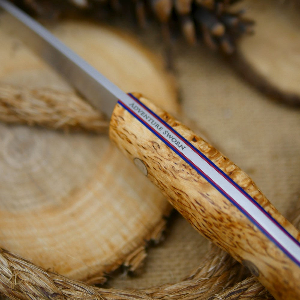 An Adventure Sworn Mountaineer bushcraft knife with karelian birch handle scales and thin blue and red liners.