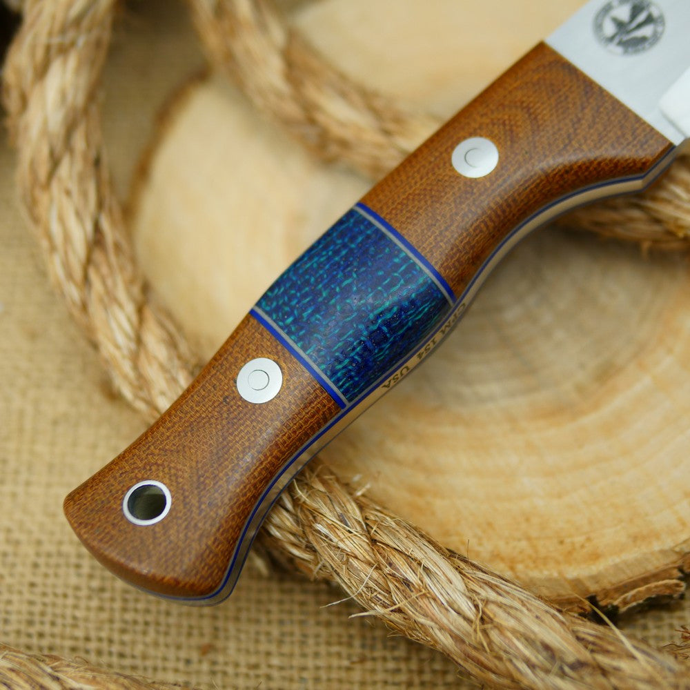 An Adventure Sworn bushcraft knife with natural brown canvas micarta handle scales and navy blue burlap spacer.